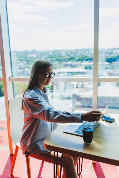 Uśmiechnięta studentka w okularach, ciesząca się oglądaniem filmu online na laptopie w czasie wolnym w przytulnej przestrzeni coworkingowej szczęśliwa freelancerka rozmawiająca z przyjaciółką w mediach społecznościowych udostępniająca zdjęcia profilowe