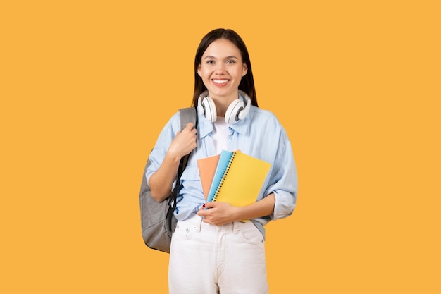 Uśmiechnięta studentka z notatnikami i plecakiem na żółtym tle
