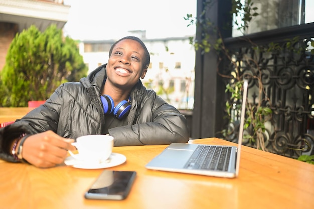 Uśmiechnięta szczęśliwa afrykańska czarna krótkowłosa studentka w czarnej puchowej kurtce z niebieskimi słuchawkami