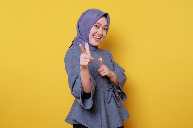 Uśmiechnięta szczęśliwa azjatycka kobieta nosząca hidżab z palcem wskazującym na jasnożółtym tle transparentu