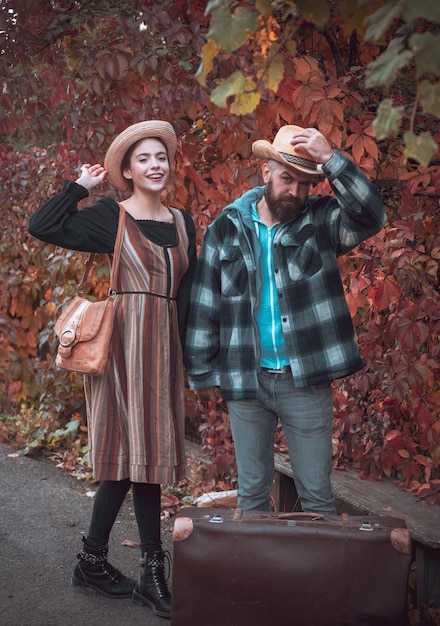 Uśmiechnięta szczęśliwa dziewczyna i brodaty mężczyzna w kapeluszu z dużym vintage wyglądającym facetem w torbie w koszuli w kratę i