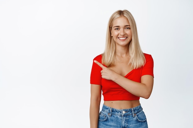 Uśmiechnięta szczęśliwa dziewczyna o blond włosach i opalonej skórze pokazuje palce wskazujące reklamy na białym tle w miejscu kopii