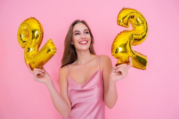 Uśmiechnięta szczęśliwa dziewczyna trzyma złoty balon foliowy na różowym tle koncepcji przyjęcia urodzinowego