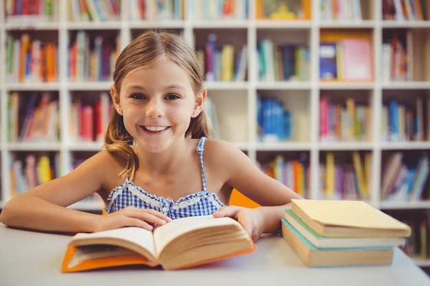 Uśmiechnięta szkolna dziewczyna czyta książkę w bibliotece