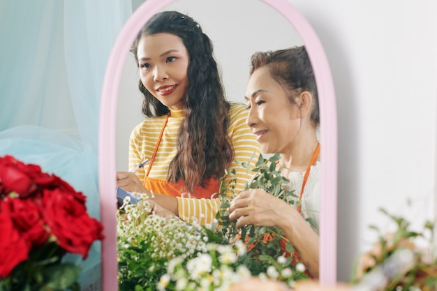 Uśmiechnięta wietnamska starsza kobieta i jej dorosła córka prowadzą rodzinny biznes i robią bukiet dla klienta, odbicie w lustrze