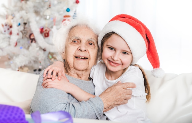 Uśmiechnięta wnuczka w santa hat przytulanie z babcią na Boże Narodzenie