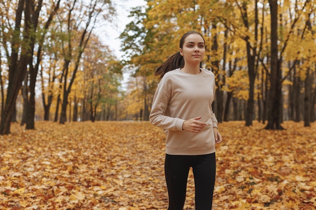Uśmiechnięta wysportowana kobieta w odzieży sportowej biegająca w parku podczas treningu jesienią
