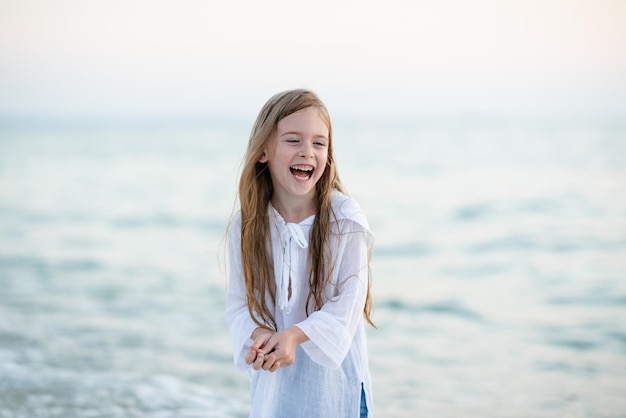 Uśmiechnięta zabawna dziewczyna 56-letnia nosi białą koszulę i dżinsowe spodnie spacer po plaży nad brzegiem morza na świeżym powietrzu Dzieciństwo Sezon letni