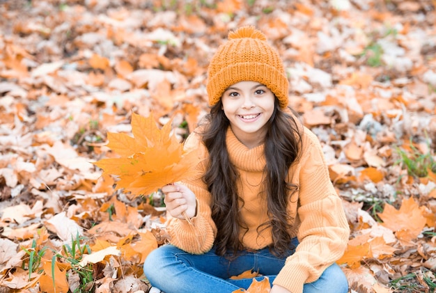 Uśmiechnięte dziecko bawiące się żółtym liściem klonu na naturalnym tle jesień natura września naturalne piękno jesień sezon modny portret nastolatki w kapeluszu trzyma jesienny liść