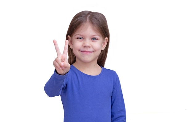 Uśmiechnięte dziecko dziecko pokazując dwa palce gest zwycięstwa na białym tle patrząc na kamery pasie w górę kaukaski dziewczynka 5 lat w kolorze niebieskim