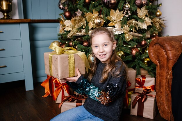 Uśmiechnięte dziecko dziewczyna trzyma w ręku prezent na Boże Narodzenie przez choinkę. Koncepcja Bożego Narodzenia.