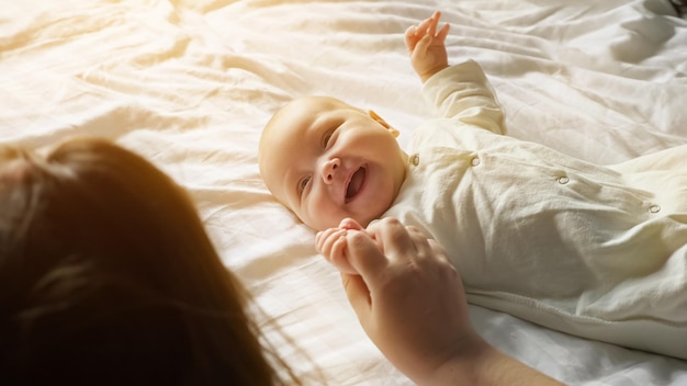 Uśmiechnięte dziecko leży na białym prześcieradle, ciesząc się uwagą mamy