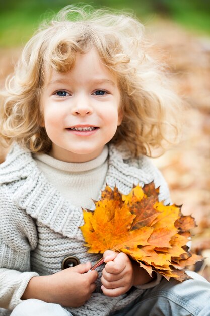 Uśmiechnięte dziecko siedzące na żółtych liściach klonu w jesiennym parku
