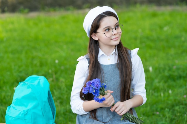 Uśmiechnięte dziecko w okularach z plecakiem trzyma kwiaty na dzień nauczyciela