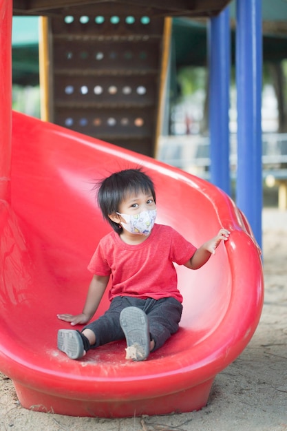 Uśmiechnięte dziecko z Azji bawiące się na suwaku zabawkowym placu zabaw na świeżym powietrzu szczęśliwe dziecko w wieku przedszkolnym bawiące się podczas zabawy na wyposażeniu placu zabaw w ciągu dnia w lecie