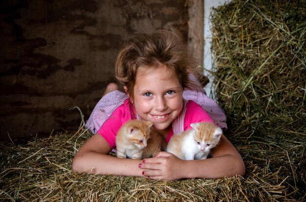 Zdjęcie uśmiechnięte dziecko z kociakami pozującymi w stodołach na bałkach słomy