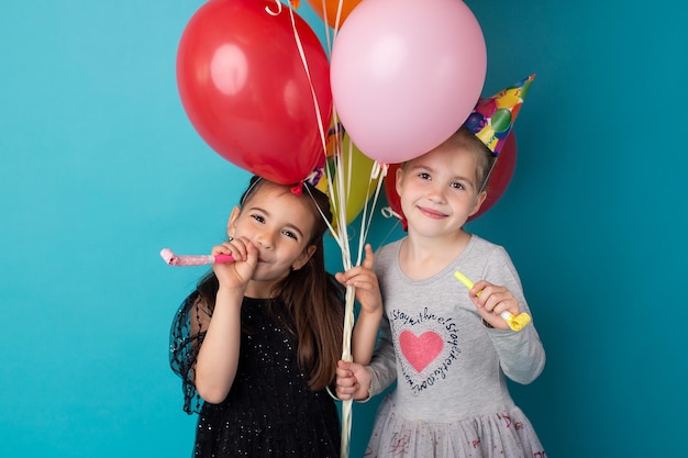 Uśmiechnięte urocze małe dziewczynki pozują z kolorowymi balonami na niebieskim tle
