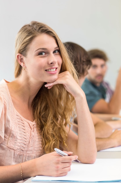 Uśmiechnięte żeńskiego ucznia writing notatki w sala lekcyjnej