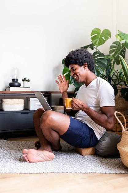 Uśmiechnięty Afroamerykanin macha witam podczas rozmowy wideo za pomocą laptopa z kawą w domu Vertical
