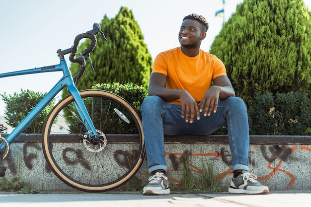 Uśmiechnięty afroamerykański mężczyzna oddala się, odpoczywając z rowerem na ulicy po jazdzie
