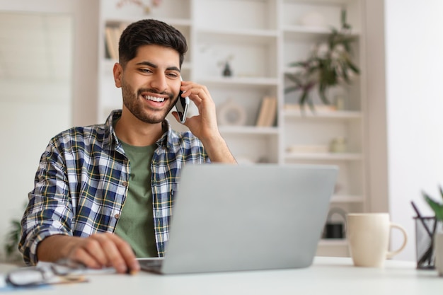 Uśmiechnięty Arab pracujący i rozmawiający przez telefon w domu