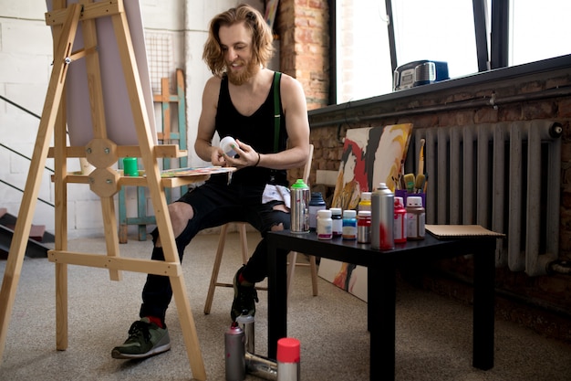 Zdjęcie uśmiechnięty artysta siedzący przy sztaludze