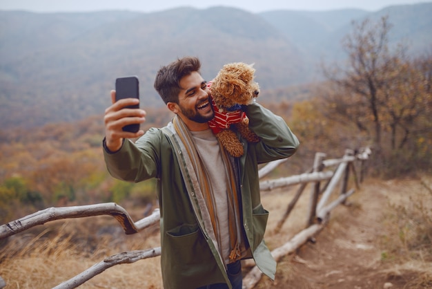 Uśmiechnięty atrakcyjny biegowy mężczyzna w płaszczu bierze selfie z psem. Jesienny czas.