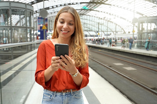 Uśmiechnięty, atrakcyjny brazylijski pasażer podróżujący kupuje bilet online za pomocą smartfona na dworcu kolejowym