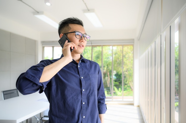 Uśmiechnięty Azjatycki Biznesmen Stojący Przy Oknie I Rozmawiający Przez Telefon