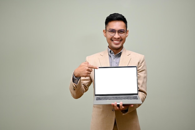 Uśmiechnięty azjatycki biznesmen wskazujący palcem na ekran laptopa stojący na zielonym tle