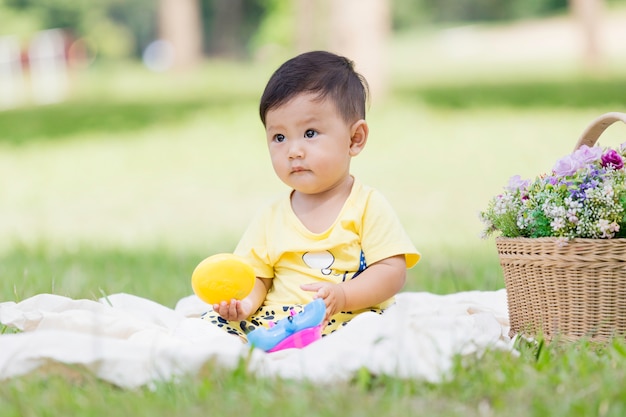 Uśmiechnięty azjatycki chłopiec czarne włosy i oczy malucha siedzieć na białym Bawełna w zielonej trawie sam i grając zabawki.