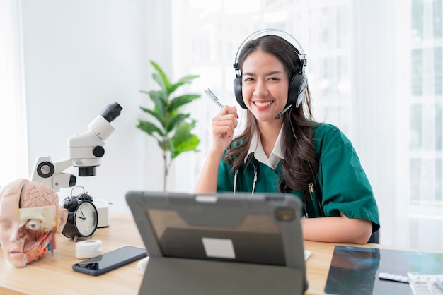 Uśmiechnięty azjatycki lekarz nosi słuchawkową rozmowę z pacjentem online telemedycyna na odległość wsparcie opieki zdrowotnej conceptasia kobieta lekarz osing tablet do zdrowia rozmowa wideo z chorymi ludźmi z domu