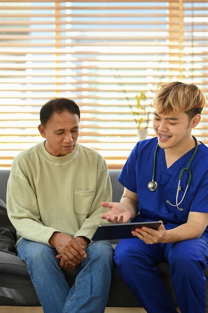 Uśmiechnięty azjatycki lekarz rozmawiający i wyjaśniający wynik testu starszemu pacjentowi podczas wizyty domowej Koncepcja opieki zdrowotnej w podeszłym wieku
