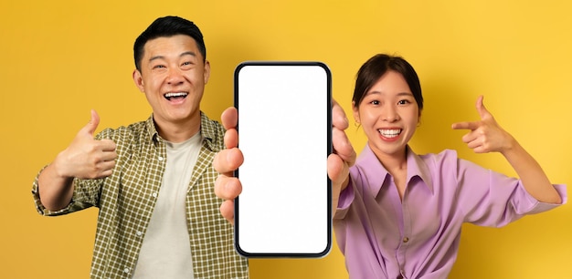Uśmiechnięty azjatycki mężczyzna i kobieta demonstrujący pusty smartfon z dużym białym ekranem