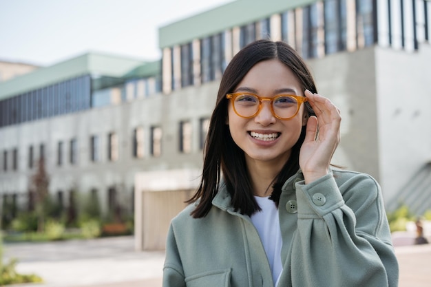 Uśmiechnięty azjatycki student noszący stylowe okulary stojący w kampusie uniwersyteckim Koncepcja edukacji
