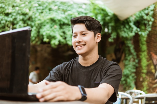 Uśmiechnięty azjatykci młody człowiek używa laptop