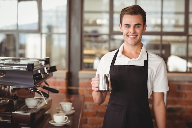 Uśmiechnięty barista trzyma dzbanek z mlekiem