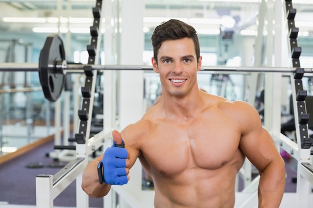 Uśmiechnięty bez koszuli mięśniowy mężczyzna daje aprobatom w gym