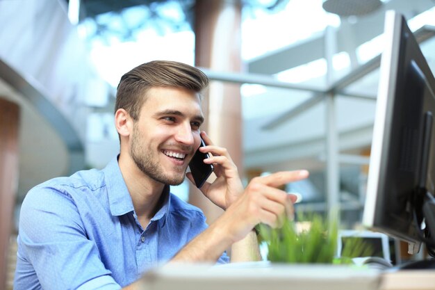 Uśmiechnięty biznesmen siedzi i używa telefonu komórkowego w biurze