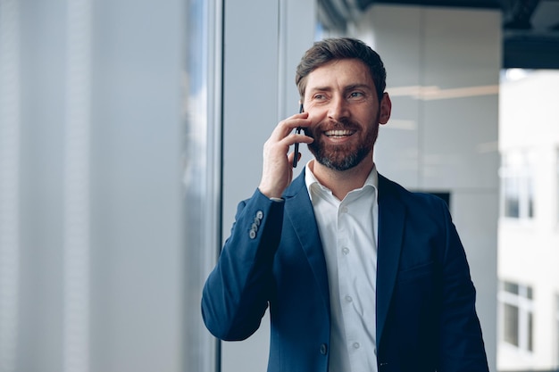 Uśmiechnięty biznesmen używa telefonu komórkowego, aby zadzwonić do swojego partnera biznesowego podczas pracy w biurze