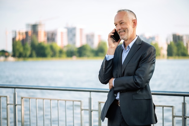 Uśmiechnięty biznesmen w szarym garniturze ze smartfonem.