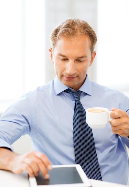 uśmiechnięty biznesmen z komputerem typu tablet pijący kawę w biurze
