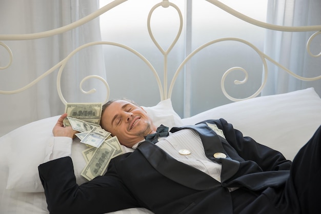 Zdjęcie uśmiechnięty biznesmen z papierowymi monetami leżący w łóżku w domu