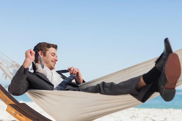 Uśmiechnięty biznesmena lying on the beach w hamock bierze daleko jego krawat