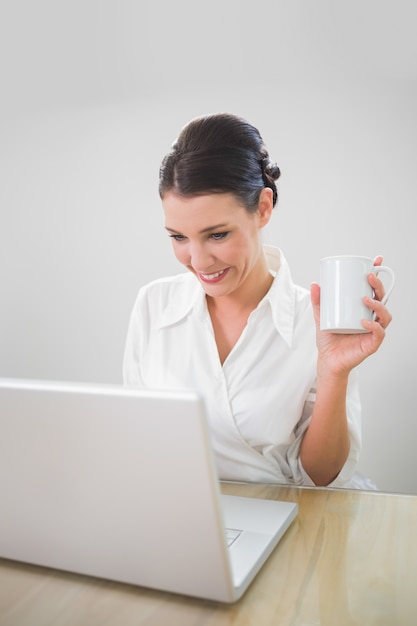 Uśmiechnięty bizneswoman pracuje na laptopu mienia kawie