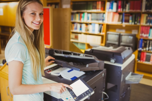 Zdjęcie uśmiechnięty blondynka uczeń robi kopii w bibliotece