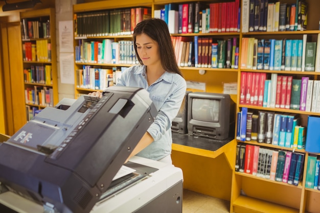 Uśmiechnięty brunetka uczeń robi kopii w bibliotece