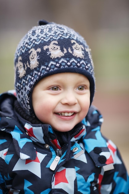 Uśmiechnięty chłopiec w ciepłych ubraniach patrzy w inną stronę.