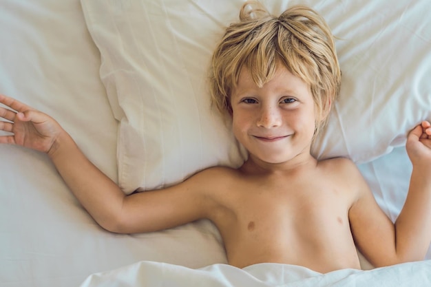 Uśmiechnięty chłopiec w łóżku budzi się w swoim łóżku
