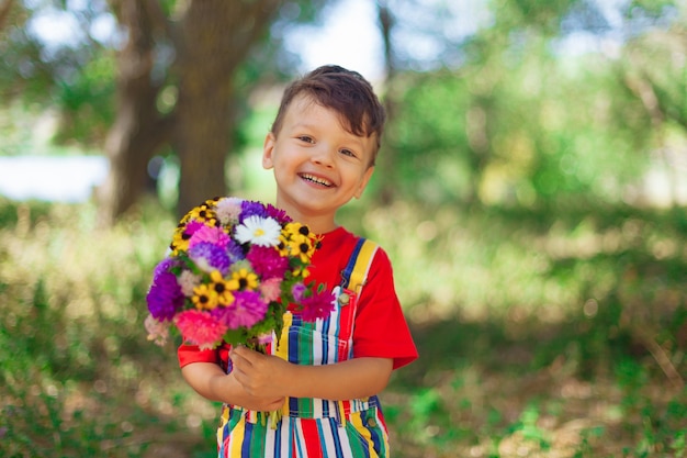 Uśmiechnięty chłopiec z bukietem polnych kwiatów niespodzianka dla mamy na wakacjach dziecko z kwiatami w ...